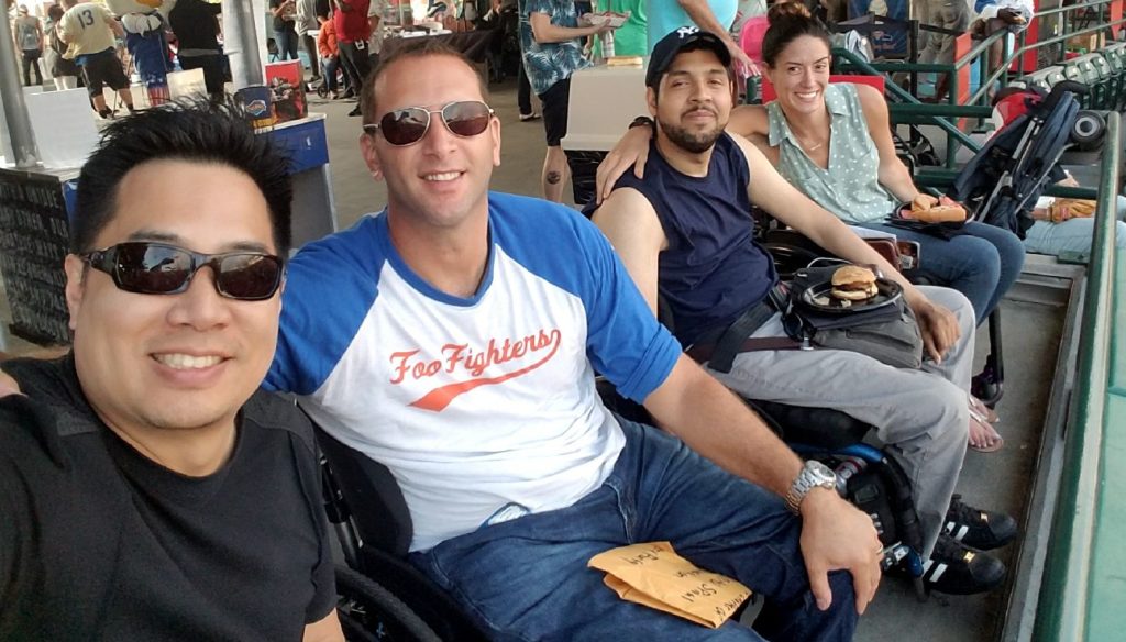 3 men and a woman in wheelchairs at a baseball game.